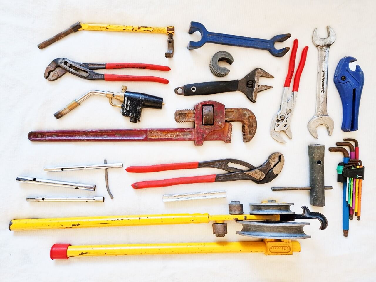 a flat lay of plumbing tools including wrenches and a pipe bender, used across the Billy The Plumber blog